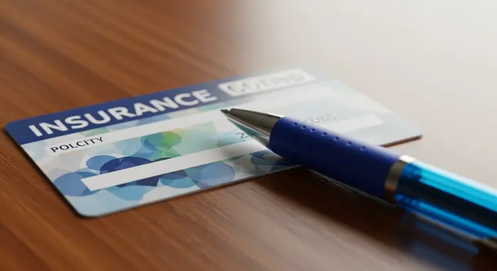 Nahaufnahme einer Versichertenkarte auf einem Holztisch neben einem Kugelschreiber; neutrale Darstellung ohne lesbare persönliche Daten; klares, weiches Licht.