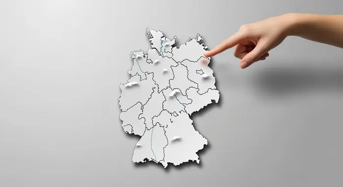 Symbolische Deutschlandkarte aus Papier ohne Beschriftungen; Hand deutet auf den Norden; neutraler Hintergrund.