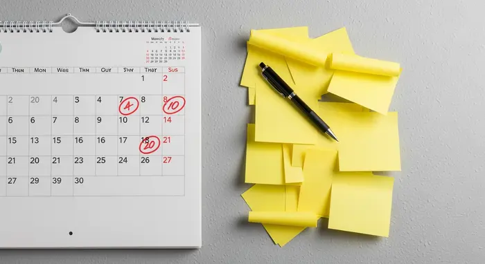 Wandkalender und Notizzettel: Rot markierte Termine, daneben Kugelschreiber; neutrale, textfreie Darstellung.