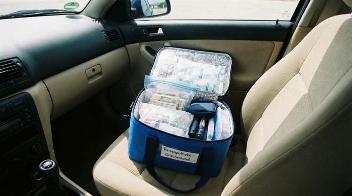 Eine kleine, blaue Isoliertasche liegt geöffnet auf dem Beifahrersitz eines Autos. Darin befinden sich sicher verpackte Medikamente für eine Reise.