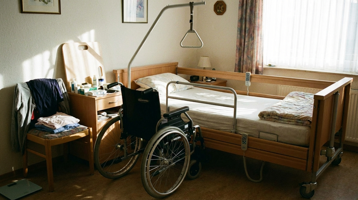 Rollstuhl neben einem Bett, der die eingeschränkte Mobilität verdeutlicht