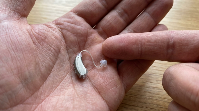 Filigranes Ex-Hörer-Gerät (RIC) in einer Hand, Größenvergleich zur Fingerspitze verdeutlicht die geringe Größe.