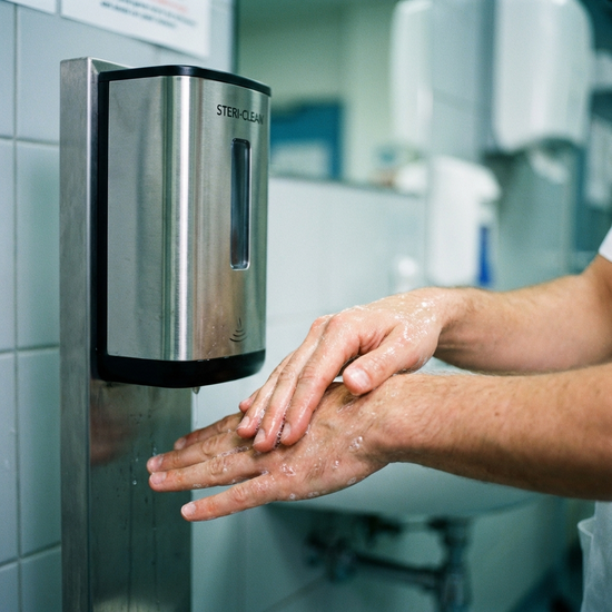 Person desinfiziert sich gründlich die Hände, Fokus auf Hände und Desinfektionsmittelspender