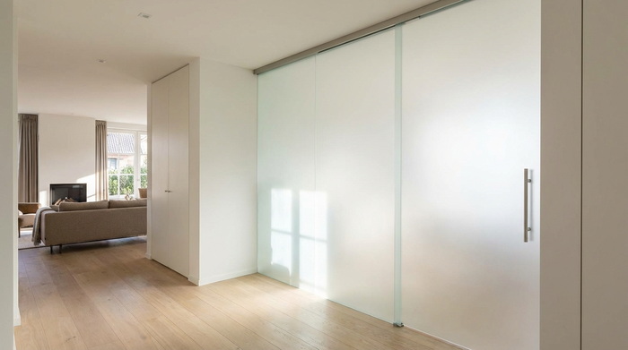 Breite, schwellenlose Schiebetür aus satiniertem Glas zwischen Flur und Wohnzimmer.