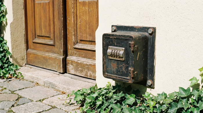 Massiver, kleiner Schlüsseltresor aus Metall mit Zahlenschloss, sicher montiert an einer hellen Hauswand neben einer Haustür