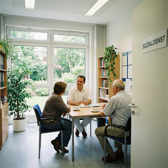 Krankenhaus-Sozialarbeiter im Gespräch mit Angehörigen in einem hellen Büro