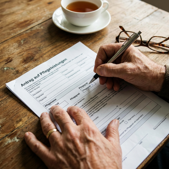 Nahaufnahme von Händen, die ein Formular zur Pflegegrad-Beantragung ausfüllen
