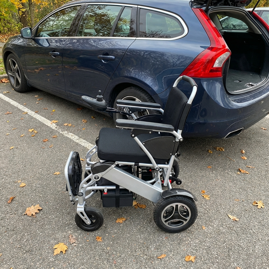 Zusammengeklappter leichter Elektrorollstuhl aus Aluminium neben einem Auto