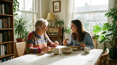 Lächelnde Seniorin unterhält sich angeregt mit ihrer Enkelin am Esstisch in einem hellen Raum
