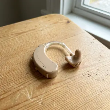 Klassisches Hinter-dem-Ohr-Hörgerät liegt auf einem hellen Holztisch