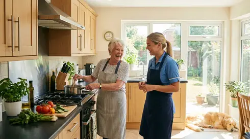 Pflegekraft kocht gemeinsam mit einer Seniorin in einer hellen Küche