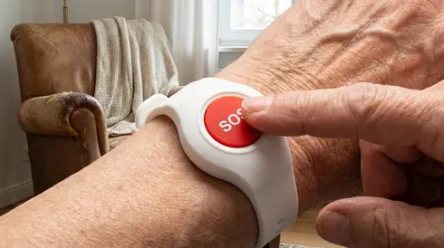 Ein Finger drückt zielgerichtet den großen roten Knopf eines Hausnotruf-Senders, der als Armband getragen wird.