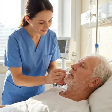 Pflegekraft befeuchtet behutsam die Lippen eines älteren Patienten mit einem Stäbchen