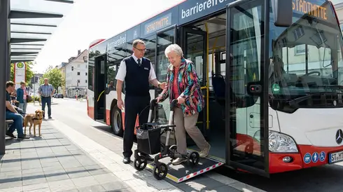 Seniorin steigt mit Hilfe einer Rampe in einen barrierefreien Bus ein