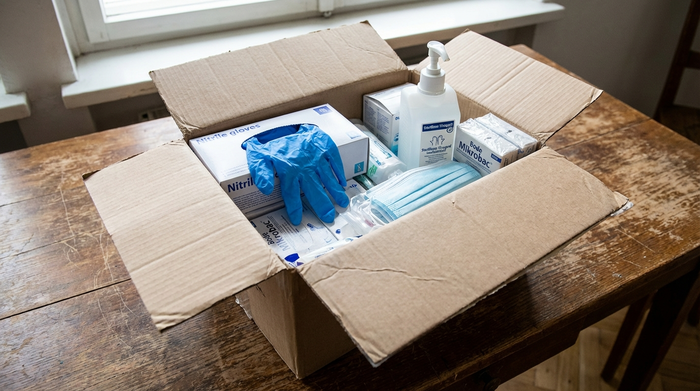 Geöffnetes Paket mit Pflegehilfsmitteln wie Einmalhandschuhen und Desinfektionsmittel auf einem Tisch.