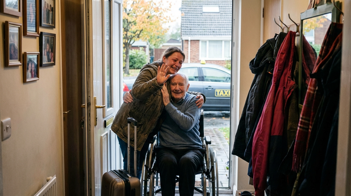 Pflegende Angehörige verabschiedet sich mit einem Koffer an der Tür