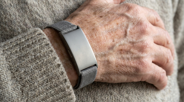 Nahaufnahme eines unauffälligen Hausnotruf-Armbands am Handgelenk eines Seniors