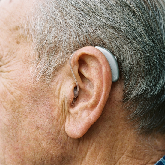 Nahaufnahme eines modernen, unauffälligen Hörgeräts hinter dem Ohr eines Seniors