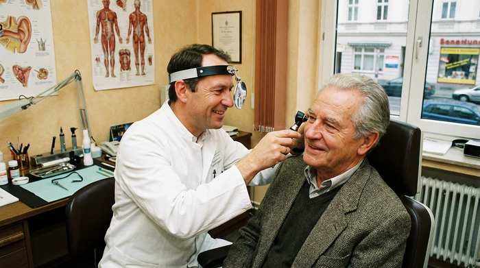 Hals-Nasen-Ohren-Arzt untersucht freundlich das Ohr eines älteren Patienten