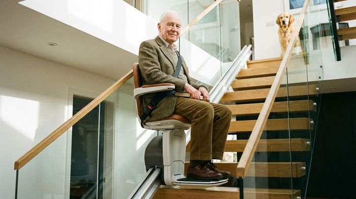 Älterer Herr sitzt entspannt und sicher auf einem modernen Treppenlift während der Fahrt nach oben