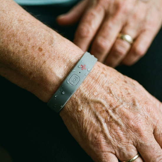 Nahaufnahme eines unauffälligen, wasserdichten Hausnotruf-Armbands am Handgelenk eines Seniors