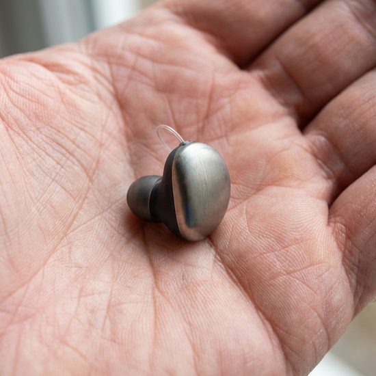 Modernes, winziges Im-Ohr-Hörgerät auf der Handfläche einer Person