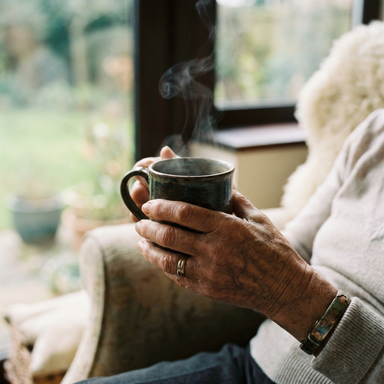 Hände einer älteren Frau, die behutsam eine warme Tasse Tee hält