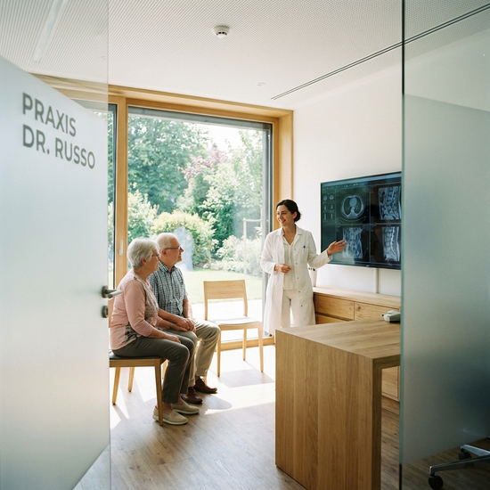 Facharzt im Gespräch mit einem älteren Ehepaar in einer modernen Praxis