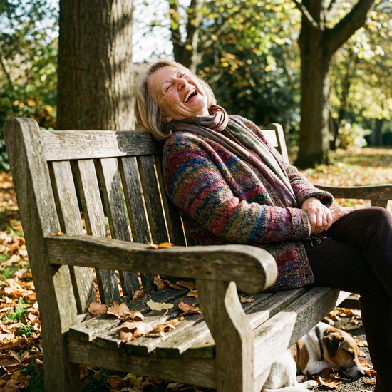 Ältere Dame lacht befreit und entspannt auf einer Parkbank