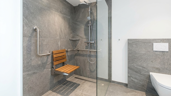 Bodengleiche Dusche mit fest installiertem Duschklappsitz und Haltegriff