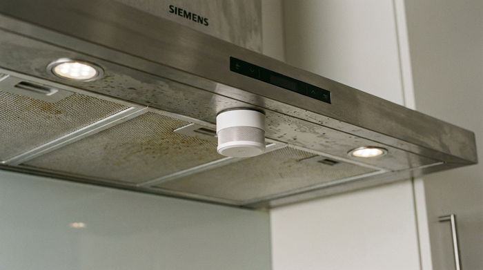 Nahaufnahme eines kleinen weißen Sensors, der dezent unter einer Dunstabzugshaube montiert ist