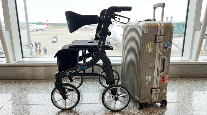 Kompakt gefalteter Reiserollator steht neben einem Reisekoffer am Flughafen