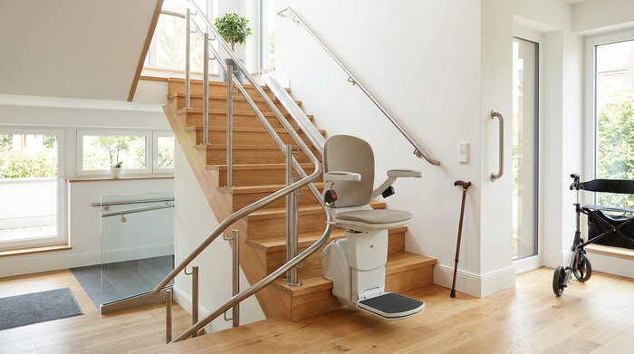 Ein moderner, eleganter Treppenlift gleitet eine helle Holztreppe in einem gepflegten Einfamilienhaus hinauf. Die Umgebung ist barrierefrei und sicher gestaltet. Fokus auf Mobilitätshilfen, realistisch ohne Text.