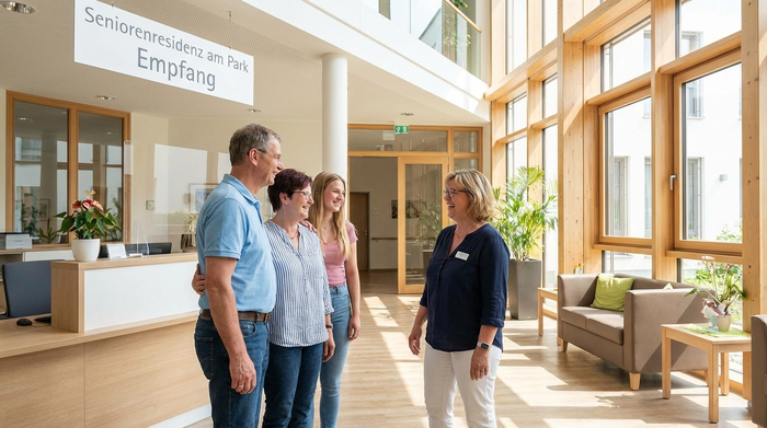 Eine freundliche Pflegedienstleitung im Gespräch mit einer interessierten Familie in einem hellen, modernen Empfangsbereich eines Pflegeheims. Offene Körpersprache, Vertrauen ausstrahlend, realistisch.