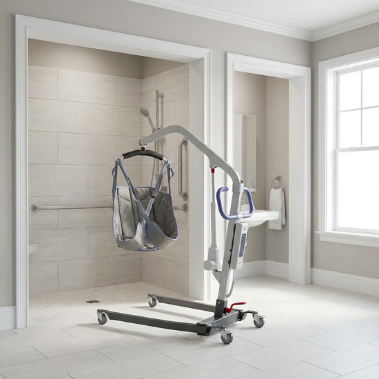 Ein mobiles Patientenlifter-System steht in einem geräumigen, barrierefreien Badezimmer mit hellen Fliesen, bereit für den sicheren Transfer in eine bodengleiche Dusche.