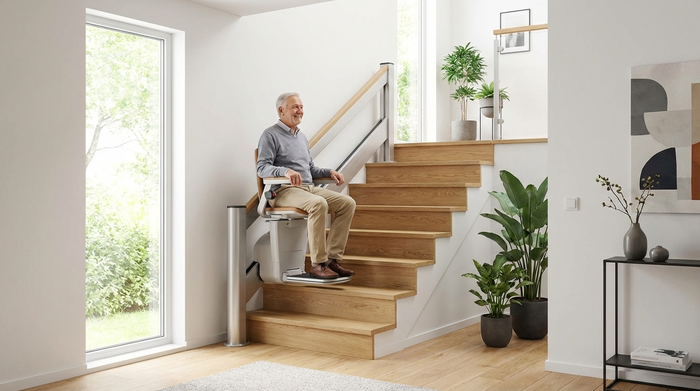 Ein moderner, eleganter Treppenlift in einem gepflegten, hellen Treppenhaus eines Einfamilienhauses. Ein älterer Herr fährt sicher und entspannt nach oben.