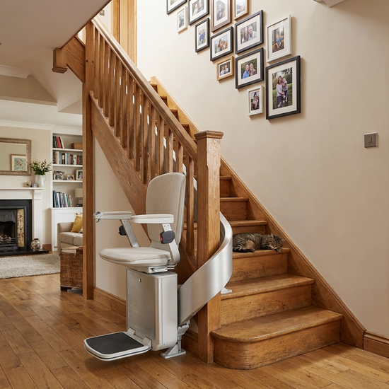 Ein eleganter, moderner Treppenlift ist an einer Holztreppe in einem gepflegten Einfamilienhaus montiert. Das Haus wirkt gemütlich und einladend, mit Familienfotos an der Wand entlang der Treppe.