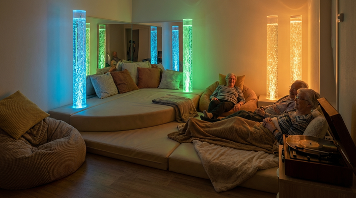 Ein gemütlicher Snoezelen-Raum mit gedimmtem Licht, weichen Liegelandschaften und sanft leuchtenden Wassersäulen. Eine ruhige, entspannende Umgebung für Senioren ohne ablenkende Reize.