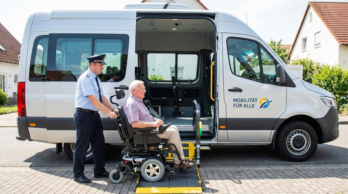 Ein moderner Behindertentransportwagen mit ausgefahrener hydraulischer Hebebühne. Ein Fahrer schiebt einen Senior im Rollstuhl sicher und ruhig in den geräumigen, hellen Fahrzeuginnenraum.
