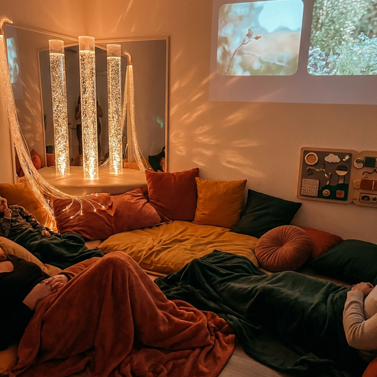 Ein gemütlicher Snoezelen-Raum mit gedimmtem Licht, sanft leuchtenden Wassersäulen und bequemen Liegekissen. Eine ruhige, entspannende Atmosphäre, warme Farben, realistisch.