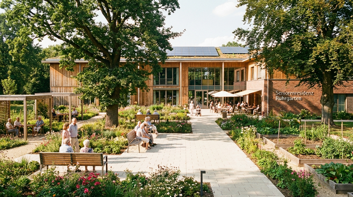 Eine moderne, einladende Außenansicht einer Seniorenresidenz im Ruhrgebiet an einem sonnigen Tag. Gepflegter Garten mit alten Bäumen, barrierefreie Wege, gemütliche Sitzbänke.