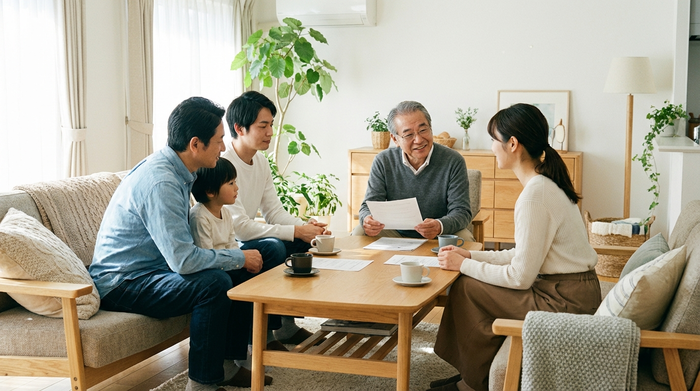 Eine Familie sitzt gemeinsam mit einem älteren Angehörigen am Wohnzimmertisch und bespricht ruhig Dokumente. Vertrauensvolles Gespräch, helle und freundliche Einrichtung.