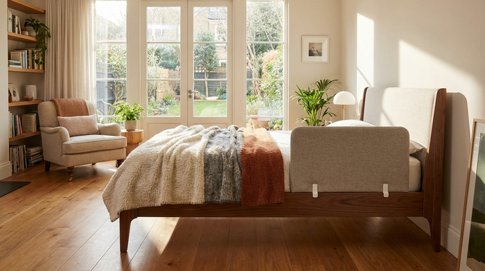 Ein sauberes, modernes Pflegebett steht aufgeräumt in einem gemütlichen, hellen Schlafzimmer mit großen Fenstern. Eine weiche Tagesdecke liegt darauf. Einladendes, sicheres und wohnliches Ambiente ohne klinische Kühle.