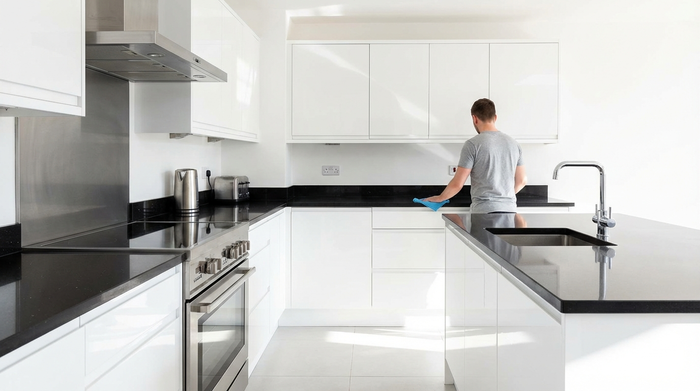 Eine blitzsaubere, moderne Küche mit glänzenden Oberflächen, im Hintergrund wischt eine Person mit einem Mikrofasertuch über die Arbeitsplatte.