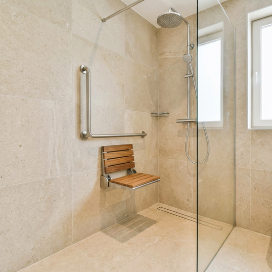 Eine moderne, barrierefreie begehbare Dusche in einem hell gefliesten Badezimmer. Ein stabiler Haltegriff und ein klappbarer Duschsitz sind an der Wand montiert. Alles wirkt sehr sauber und sicher.