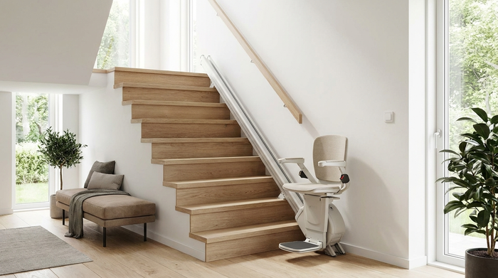 Eine moderne, helle Holztreppe in einem gepflegten Einfamilienhaus. Ein eleganter, unauffälliger Treppenlift ist an der Wand montiert. Die Umgebung wirkt sicher, barrierefrei und stilvoll eingerichtet.
