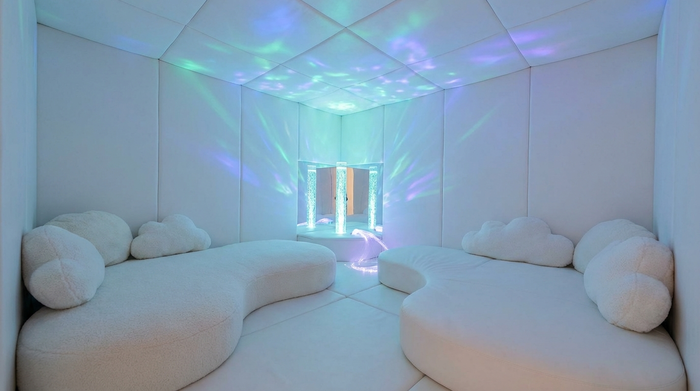 Ein komplett in Weiß gehaltener Snoezelen-Raum mit bequemen, weichen Liegelandschaften. Sanfte, farbige Lichteffekte an der Decke und eine entspannende, reizarme Atmosphäre, realistische Darstellung.