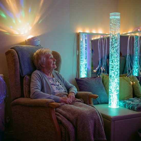 Ein gemütlicher Snoezelen-Raum mit gedimmtem, weichem Licht. Eine ältere Frau sitzt entspannt in einem bequemen Sessel und betrachtet fasziniert eine sanft blubbernde, beleuchtete Wassersäule. Ruhige, therapeutische Atmosphäre.