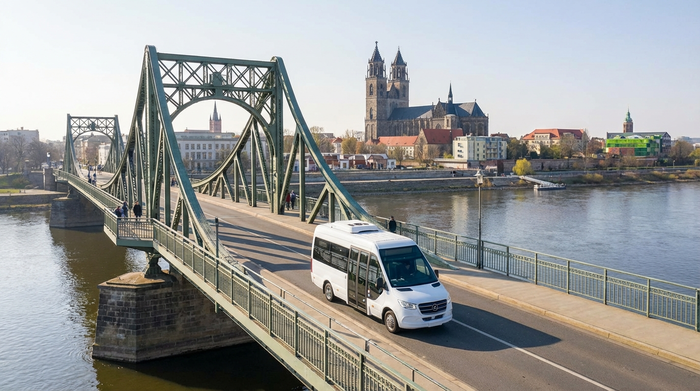 Ein moderner, weißer Kleinbus fährt an einem sonnigen Tag über eine Brücke in Magdeburg, im Hintergrund ist sanft die Elbe zu erkennen, klare und freundliche Umgebung ohne störende Texte.