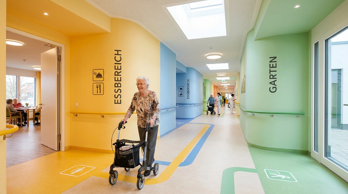 Ein farblich markierter, heller Flur in einem modernen Pflegeheim, der Demenzkranken die Orientierung erleichtert. Eine ältere Person spaziert entspannt durch den gut beleuchteten Gang ohne Sackgassen.